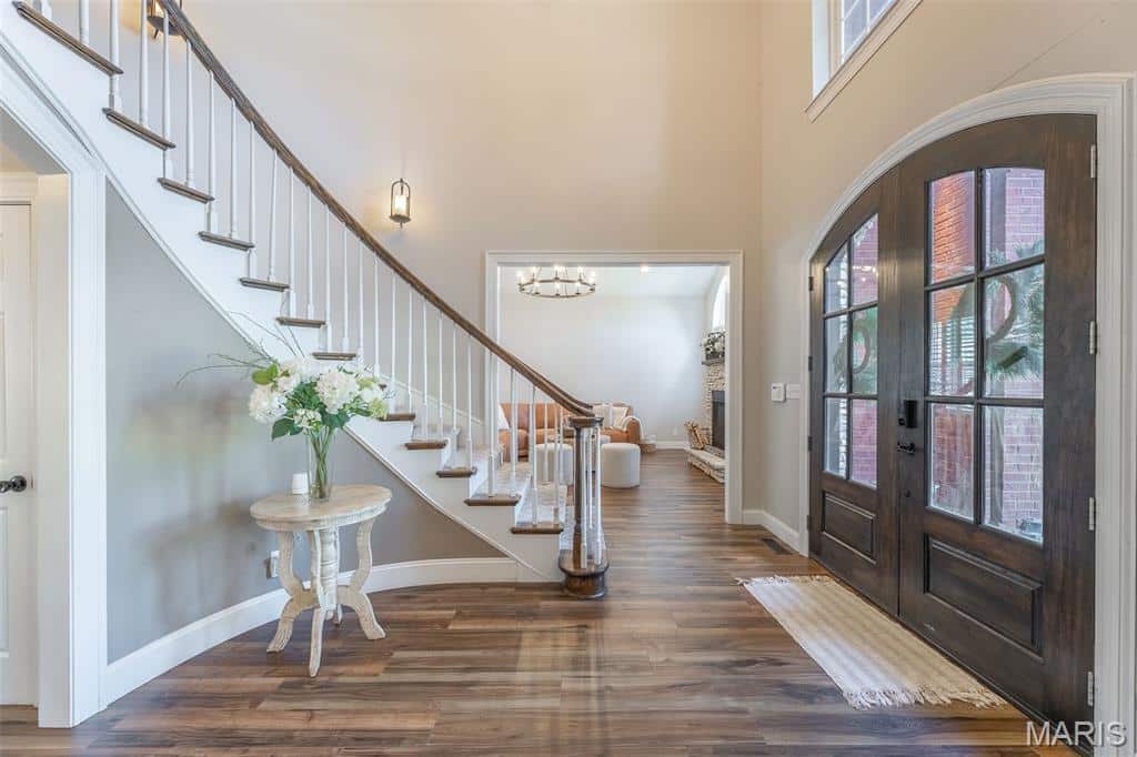 Bright entryway of 902 Paradise Lane in Poplar Bluff, Missouri, featuring double front doors, hardwood floors, a curved staircase, and a view into the living area.